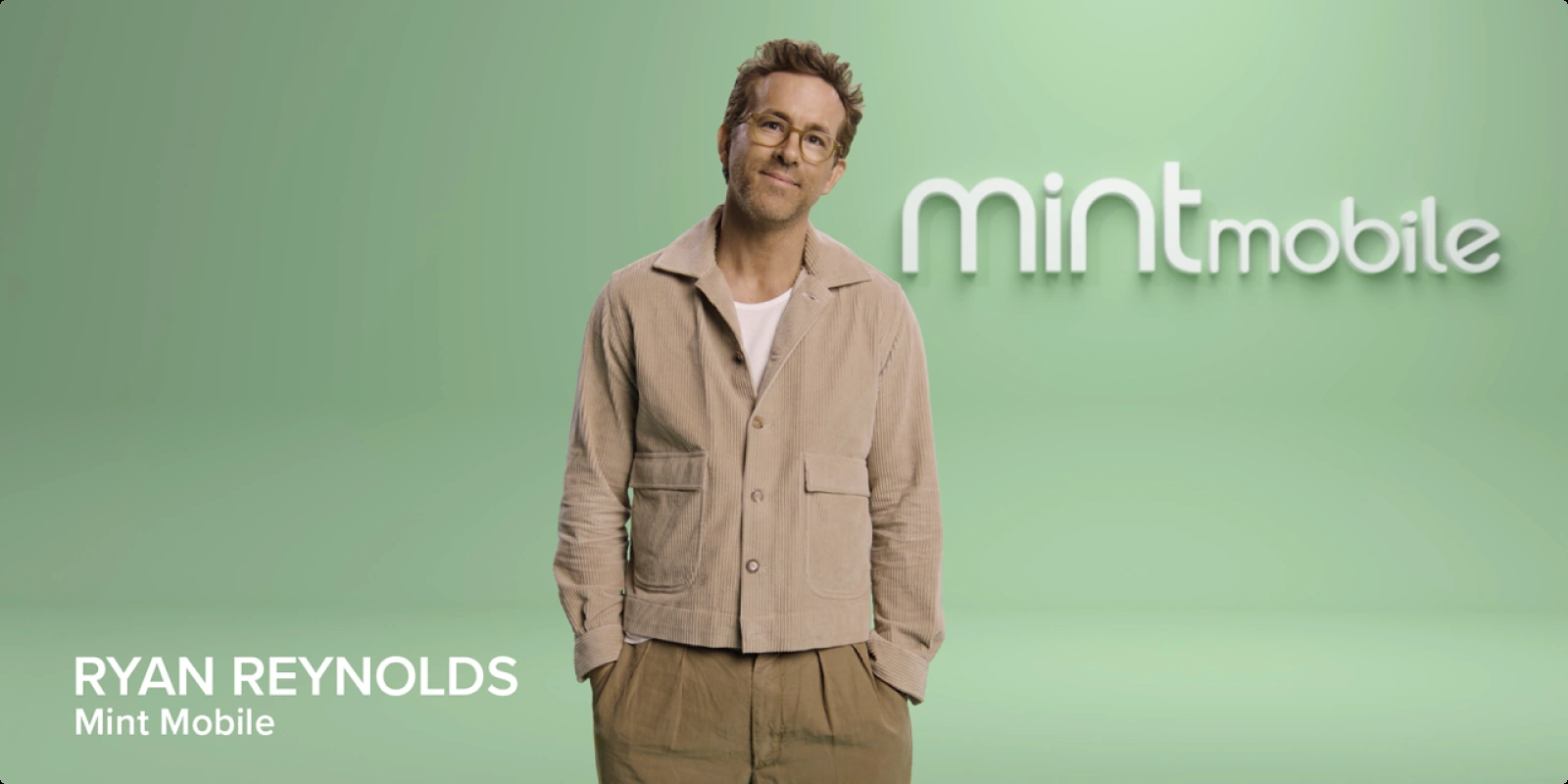 Ryan Reynolds standing next to the Mint Mobile logo in a Mint Mobile ad campaign